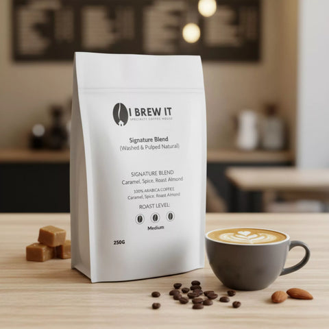 Signature Blend 250g bag with brewed cup on wooden table, warm bokeh, caramel piece and roasted almonds props.